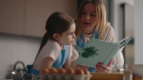 cooking-by-receipt-in-cookery-book-woman-and-little-girl-are-reading-cookbook-in-home-kitchen